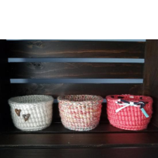 Three small crocheted baskets in soft colors sitting on a bench.