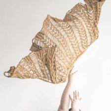 Lacy shawl thrown into the air. Design has vertical chevron-like columns with openwork from multiple needle wraps in between.