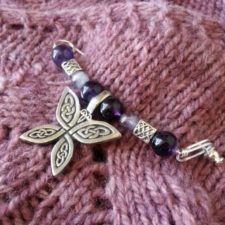 Pin is like a safety pin with a stick pin stopper. It has round, amethyst beads and pewter beads with celtic knots on them. The center has a pewter butterfly charm with knots on the wings.