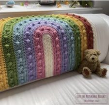 Baby blanket with curved rainbow that has same-color bobbles in each ring.