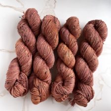 Four warm-tone tweed skeins on white marble background