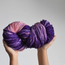 Hands hold large skein of bulky variegated yarn to the sky.