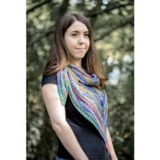 Woman in woods wears multicolor shawl that comes to a long, curved point in front. Yarnovers add openness every few rows.