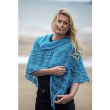 Woman on beach in large, lacy shawl.