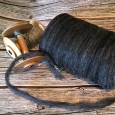 Black undyed roving and two wood spindles.