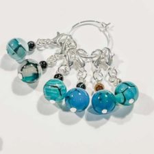 Six stitch markers with blue and black agate that looks like scales. smaller bead on top is in another color.