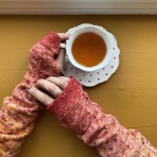 Long, crumpled fingerless mitts. Hands are holding a cup of tea.