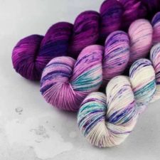 Three variegated skeins. One is deep plum tonal. One is medium plum with aqua notes. One is cream color with aqua and light plum notes.