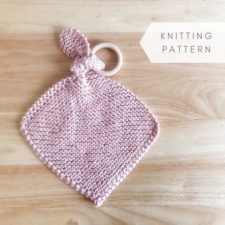 Knitted square with longer corner tied in a knot and capturing a teething ring.