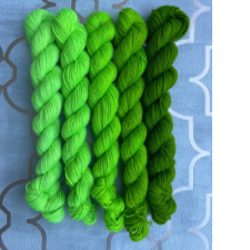 Five mini skeins ranging from fluorescent green to pine green.