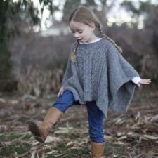 Child walks in the woods wearing a cabled rectangular poncho.