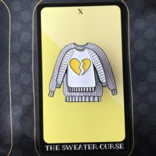 Enamel pin of a pullover with a broken heart on the front.