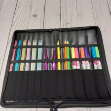 Interior of unzipped, unfolded case shows DPNs, crochet hooks and colored pencils held in place by multiple elastic bands and narrow pockets.