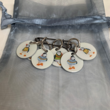 Round enamel stitch markers bearing puffins in sweaters.