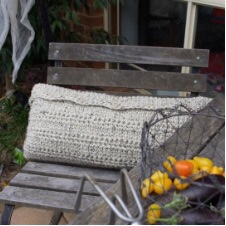 Rectangular crocheted cushion with button flap and textured body sits on garden chair.