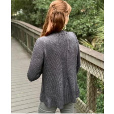 Woman wearing long sleeve cardigan. The center back of the cardigan has an almost pleated band down the length of it that gathers the cardigan slightly at the waist.