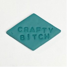Diamond-shaped clay pin with the words Crafty B!tch in all caps.