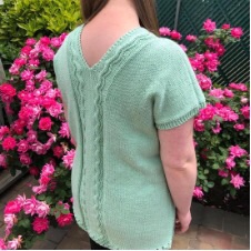 Tunic length knitted sweater with V-neck front and back. Front and back have a vertical panel with simple scalloped cables.