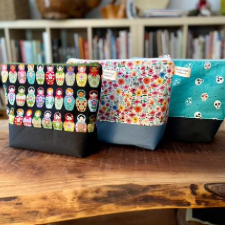 Three zippered project bags, one with Russian dolls. One with cats peeking out of flowers. One with playful skulls.