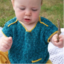 Baby waves stick while wearing crocheted top with tiny pocket.