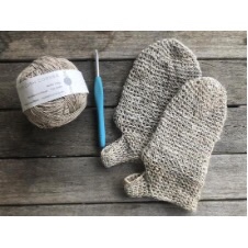 Two crocheted shower mittens in undyed yarn, plus a ball of yarn and a crochet hook.