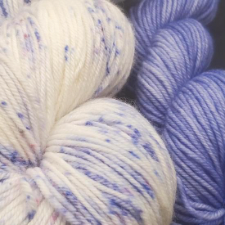 Cream yarn speckled with violet, along with a tonal mini skein of the violet.