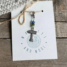 Stitch marker depicting wooden arrow sign saying “Camping.”