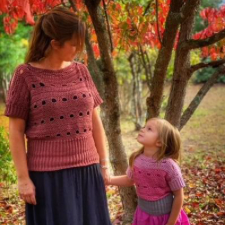 Woman and child in the woods wearing matching crocheted short-lseeve sweaters that have openwork bands.