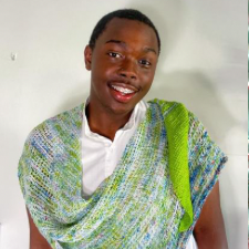 Smiling designer wears narrow crocheted boomerang shawl in bright and speckled colorway.