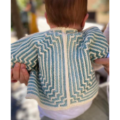 A baby, shown from the back, is wearing a two-color crochet cardigan with an intricate series of smaller and smaller squares with zigzag corners.