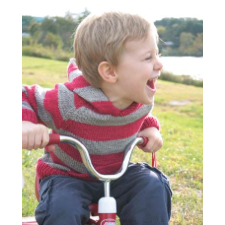 Grinning child on tricycle, wearing hoodie with wide, horizontal stripes.