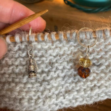 Old-fashioned lantern stitch marker in silver metal and coordinating faceted glass beads in warm tones.