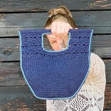 Tote with rods through the handles and a large hand opening for easy transport. Crochet bag is a half hexagon, topped by lace bars leading up to the rods.