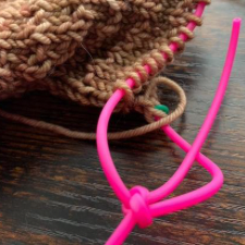 Cords through the loops of a project removed from needles. Cords are knotted together.