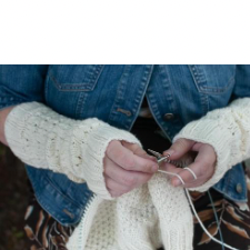 Person wearing lace and texture fingerless mitts is knitting a sweater.