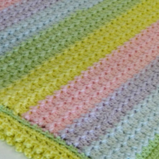 Crocheted blanket in wide stripes in various pastels. Stitches are consistent throughout, with a bobble edge.