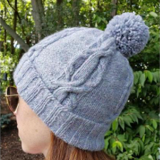 Beanie with foldup brim and pompom. Four sides of the hat have a wide, complex cable.