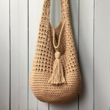 Hobo-style bag with shoulder strap and large decorative tassel at top center of the bag itself.