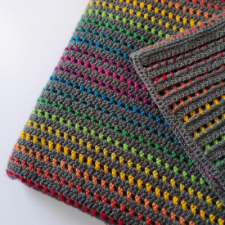 Textured blanket with gray main color and rainbow stripes between.