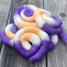 A stack of coiled rolags in a cool cantaloupe color and violet, with plenty of bright white.