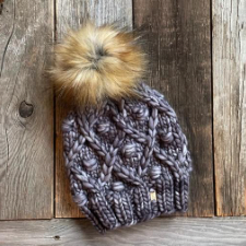 Diamond texture with a bobble in the center of each. Hat has ribbed edge and large pompom