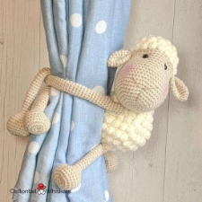 Crocheted sheep with its front legs wrapped around the curtains to hold them back.