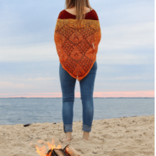 Woman standing near beach fire in lace shawl knitted in gradient. Shawl is triangular with large motifs.