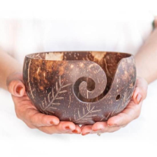 Hands cradle dark wooden bowl with yarn swirl and tiny hole options. Carved into the wood are lighter leaves.