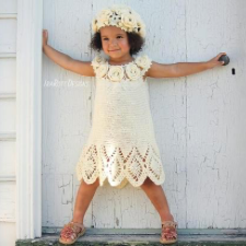 Small child in crocheted lace dress that has crocheted roses around the yoke. Roses are repeated in the hat she wears.