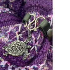 Shawl cuff where strap is joined by wavy silver wire closure. Suspended from the wire is an ornate sea turtle charm.