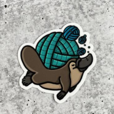 Sticker of happy platypus bearing a ball of yarn on its back.