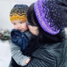 Woman holds baby. They are each wearing a hat that has a colorwork crown shape and matching confetti speckles.