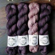 Set of yarns in deep purples and pale pink.