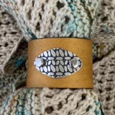 Leather cuff with metal plate engraved with crochet stitches.